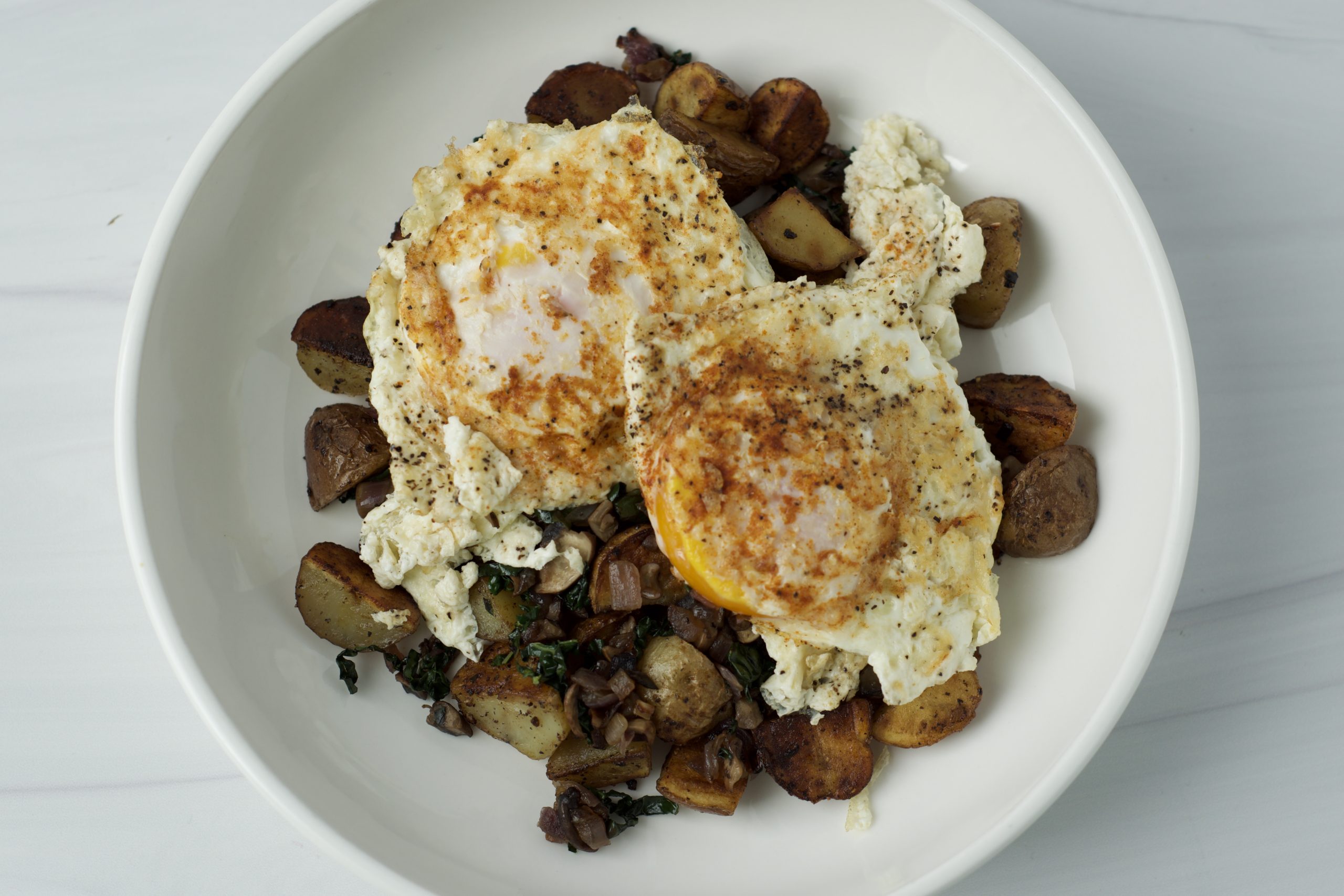Seasoned fried eggs over pan roasted red onion, mushrooms, kale and quartered mini potatoes
