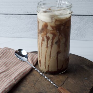 Iced latte in a glass Mason jar with glass straw on wood board