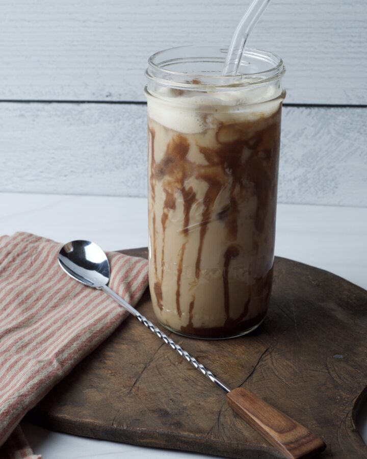 Iced latte in a glass Mason jar with glass straw on wood board